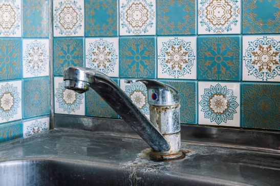 An old kitchen mixer tap in a kitchen with mosaic pattern tiles